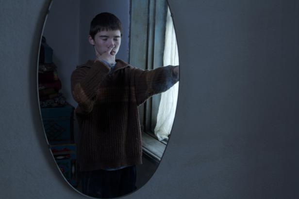 Ein junger Mann betrachtet sein Spiegelbild in einem ovalen Spiegel.