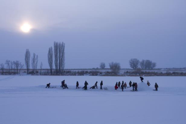 Eine Gruppe von Menschen genießt einen Wintertag mit Schlittenfahren auf einer schneebedeckten Fläche.