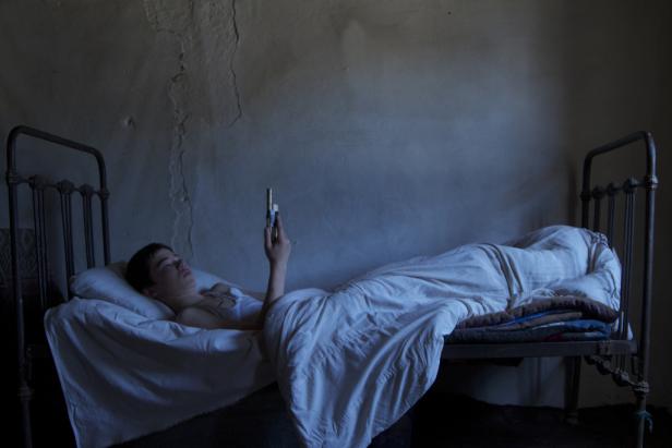 Eine junge Person liegt in einem Bett und hält ein Handy in der Hand.