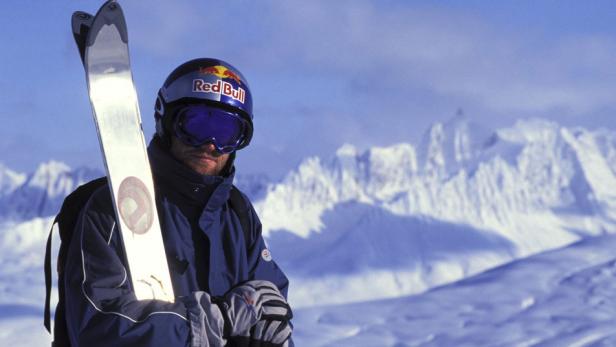 Ein Skifahrer mit Helm und Skibrille vor einer verschneiten Berglandschaft.