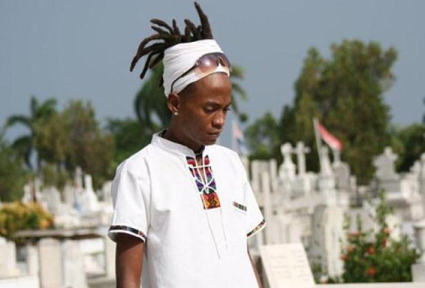 Ein Mann mit Dreadlocks, Turban und Sonnenbrille steht auf einem Friedhof.