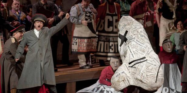 Eine Opernszene mit einem Sänger in Militäruniform und weiteren Darstellern in ungewöhnlichen Kostümen.