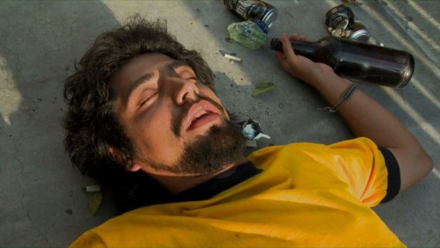 Ein bewusstloser Mann liegt mit leeren Flaschen und Zigaretten auf dem Boden.