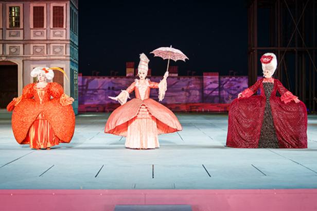 Drei Darstellerinnen in historischen Kostümen und Perücken stehen auf einer Bühne.