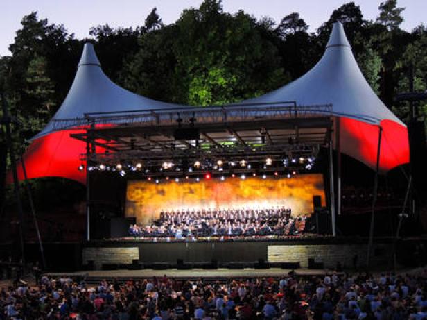 Ein Orchester und ein Chor treten vor einem großen Publikum unter einem Zelt auf.