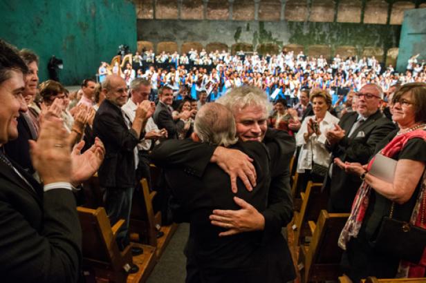 Zwei Männer umarmen sich vor einem applaudierenden Publikum.