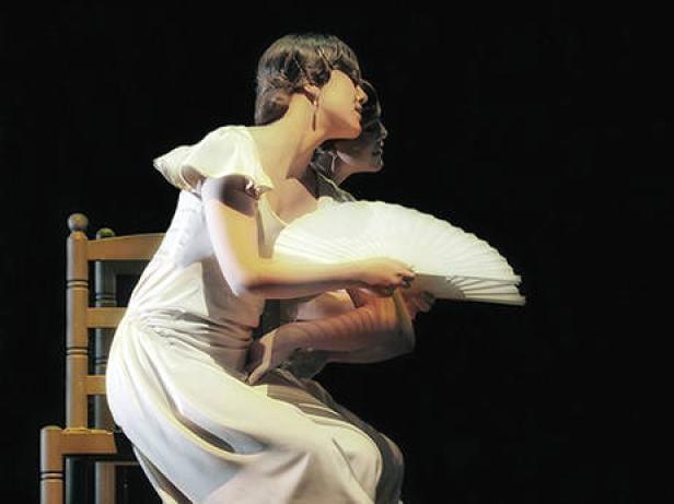 Eine Frau im weißen Kleid sitzt auf einem Stuhl und hält einen weißen Fächer.