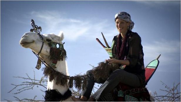 Eine Frau reitet auf einem geschmückten, weißen Kamel vor blauem Himmel.