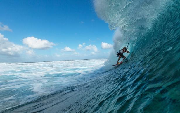 Ein Kitesurfer reitet auf einer großen Welle unter blauem Himmel.