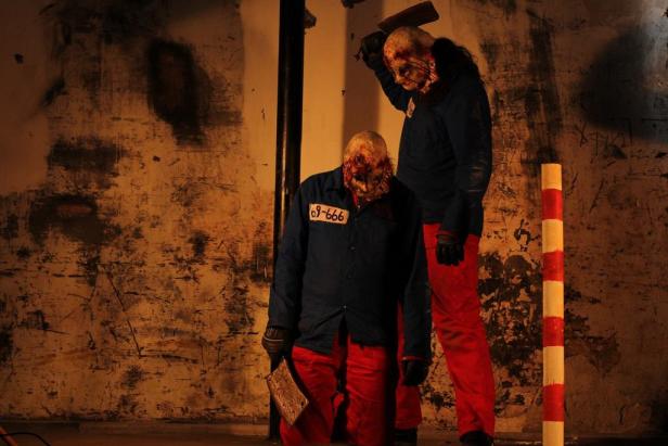 Zwei gruselige Gestalten mit Masken und Fleischerbeilen in einem dunklen Raum.