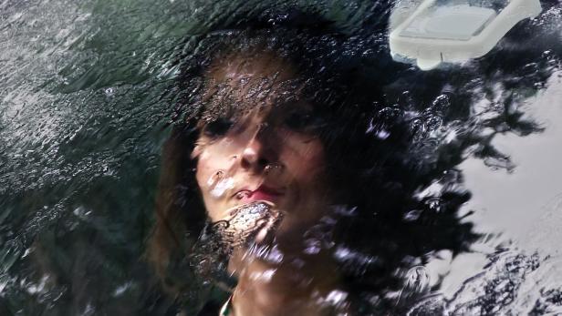 Das Gesicht einer Frau ist durch eine regennasse Autoscheibe zu sehen.