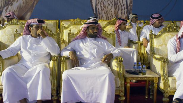 Männer in traditioneller Kleidung sitzen auf goldenen Stühlen.