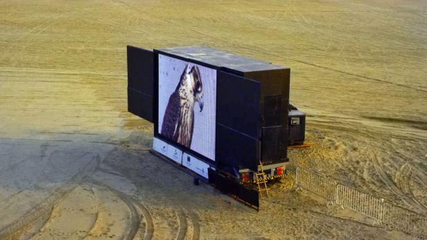 Ein großer Bildschirm auf einem LKW zeigt das Bild eines Falken in einer Wüstenlandschaft.