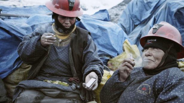Zwei Frauen mit Schutzhelmen rauchen Zigaretten vor einer Plane.
