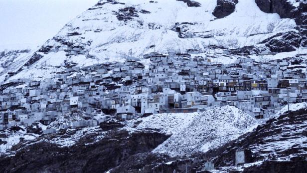 Eine dicht bebaute Siedlung schmiegt sich an einen schneebedeckten Berghang.