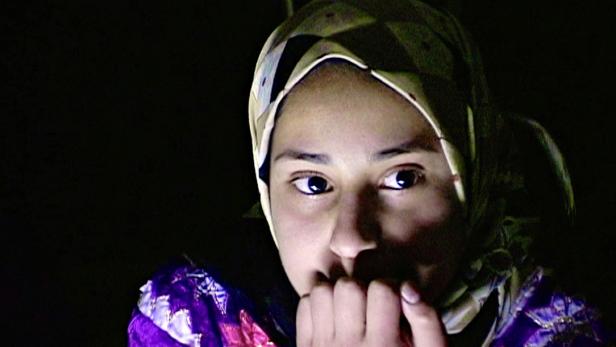 Eine junge Frau mit Kopftuch blickt in der Dunkelheit nachdenklich zur Seite.