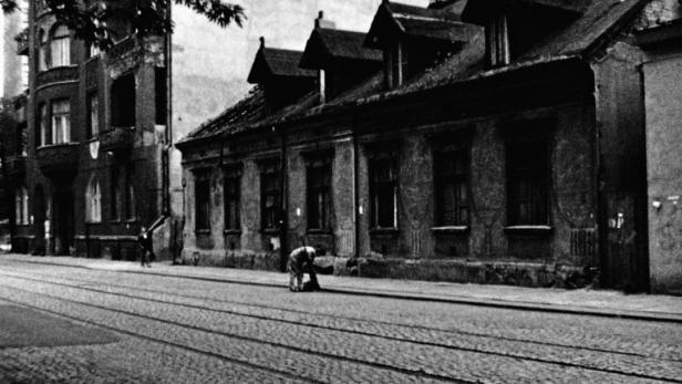 Eine ältere Frau kehrt die Straße vor alten Gebäuden in einer Stadt.