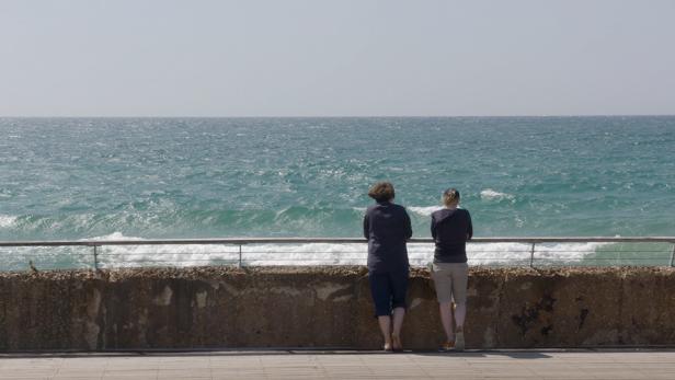 Zwei Personen stehen an einer Uferpromenade und blicken auf das Meer.