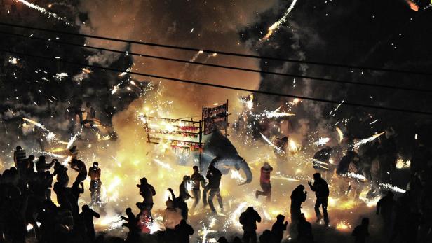 Eine Menschenmenge feiert mit Feuerwerk und einem Elefantenwagen bei Nacht.