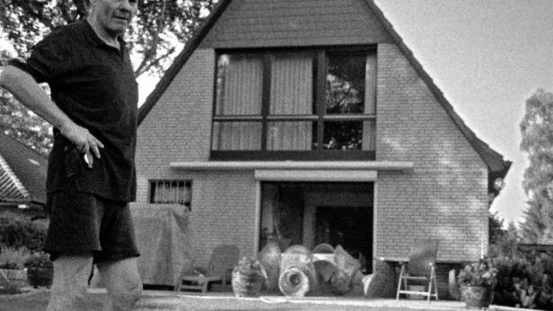 Ein Mann steht vor einem Haus mit vielen Töpferwaren im Garten.