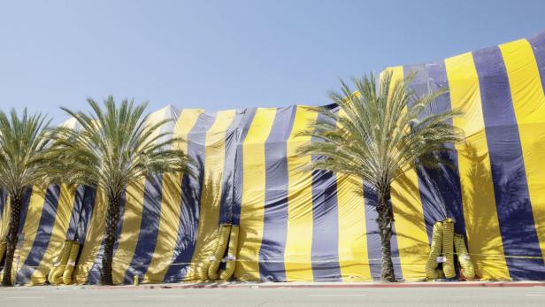Ein Gebäude ist mit einem gelb-blau gestreiften Zelt abgedeckt, flankiert von Palmen.