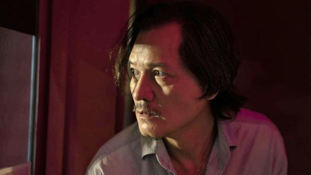 Ein Mann mit Schnurrbart blickt in einem Raum mit rotem Licht zur Seite.