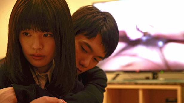 Ein junges Paar umarmt sich vor einem Fernseher.