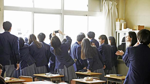 Eine Gruppe japanischer Schüler drängt sich am Fenster eines Klassenzimmers.
