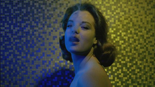 Eine Frau raucht vor einem blau und gelb gefliesten Hintergrund.