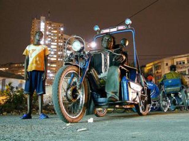 Ein Mann sitzt auf einem motorisierten Dreirad, während ein Junge daneben steht.