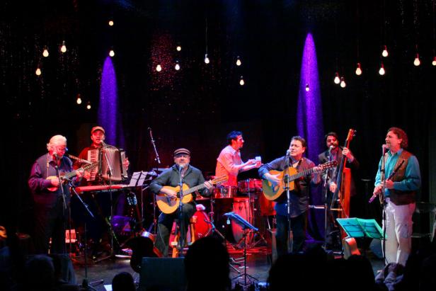 Eine Musikgruppe tritt auf einer Bühne mit Gitarren, Akkordeon und anderen Instrumenten auf.