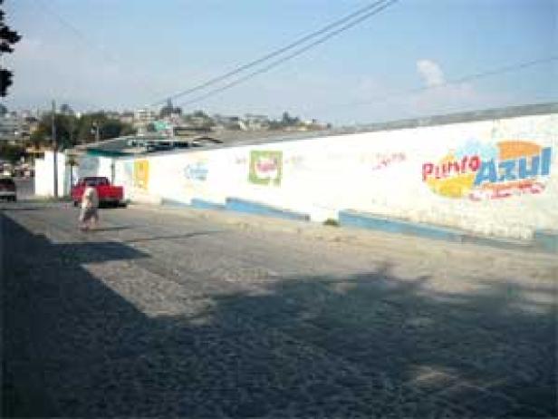 Eine Person geht an einer langen, weißen Mauer mit Werbeaufschriften vorbei.