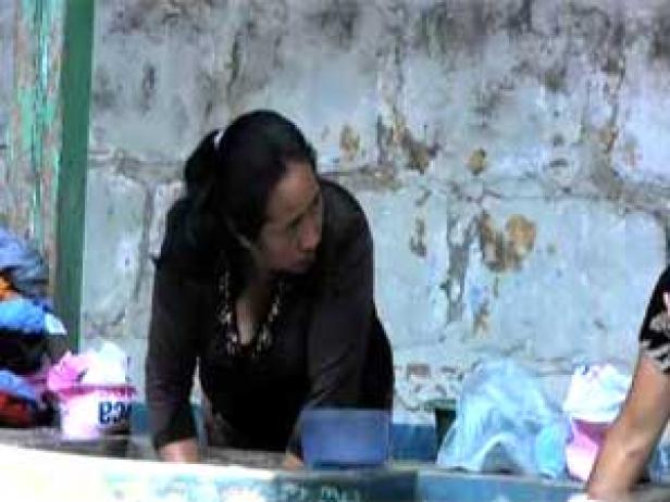 Eine Frau wäscht Kleidung in einem Waschbecken im Freien.