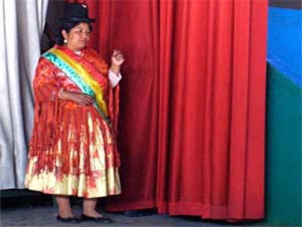 Eine Frau in traditioneller Kleidung und Hut steht vor roten Vorhängen.