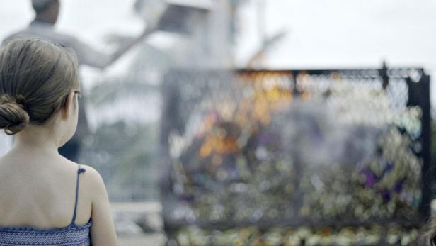 Ein Mädchen blickt auf ein Feuer, das in einem Metallbehälter brennt.