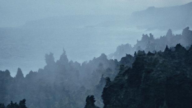 Eine neblige Berglandschaft in dunklen Blautönen.