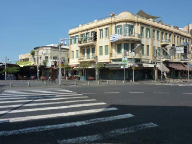Eine Straßenkreuzung mit einem gelben Eckgebäude im Bauhausstil.