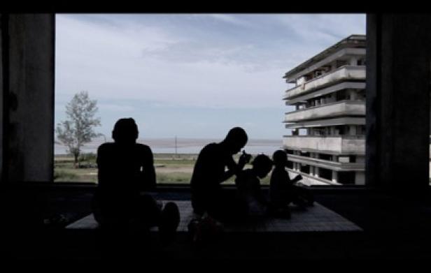 Im Schatten sitzen Menschen in einem verlassenen Gebäude mit Blick auf das Meer.