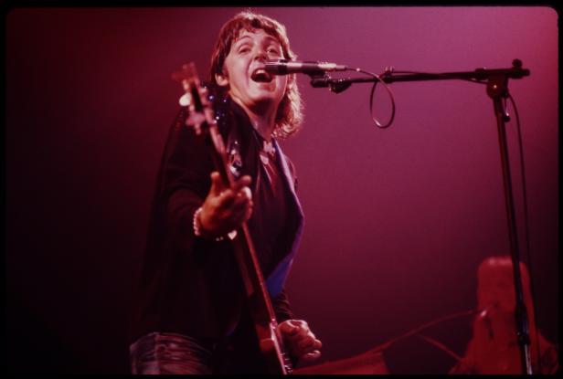 Paul McCartney spielt Gitarre und singt in ein Mikrofon auf der Bühne.