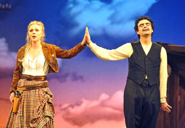 Eine Frau im Western-Outfit und ein Mann geben sich ein High-Five auf einer Theaterbühne.