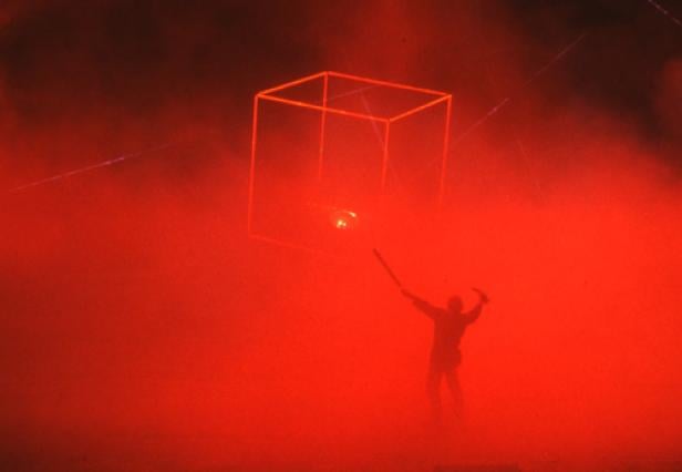 Eine Person steht in rotem Nebel unter einem leuchtenden Würfel.