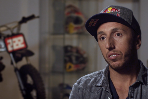 Ein Mann mit einer Red Bull-Kappe vor einem Motorrad und Helmen.