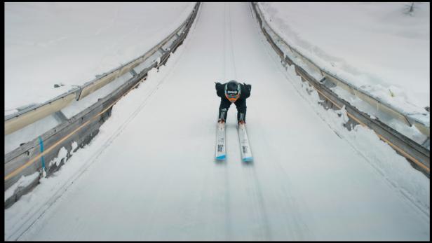 Ein Skispringer fährt einen schneebedeckten Hang hinunter.