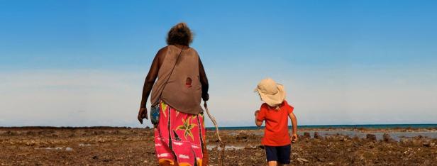Eine ältere Frau und ein Kind gehen am Strand entlang.