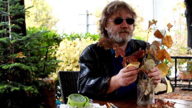 Ein Mann mit Sonnenbrille sitzt draußen und betrachtet Herbstblätter.