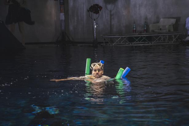 Ibrahim Aly schwimmt mit Schwimmbrille und Schwimmnudeln in einem dunklen Becken.