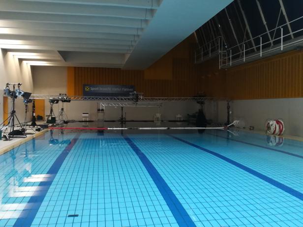 Ein Schwimmbecken mit blauen Fliesen und einer temporären Beleuchtungsanlage für Dreharbeiten.