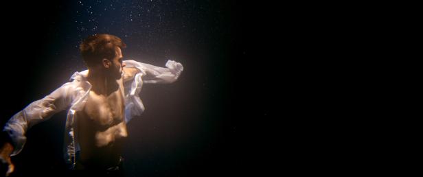 Ein Mann mit offenem Hemd taucht im dunklen Wasser.