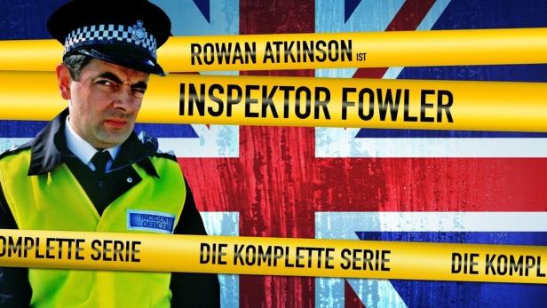 Rowan Atkinson als Inspektor Fowler vor einer britischen Flagge und Absperrband.