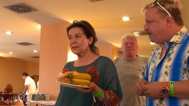 Eine Frau hält einen Teller mit Bananen und Gebäck in einem Speisesaal.